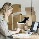 Pemilik usaha mengemas pesanan online dikelilingi bahan packing dan laptop