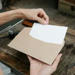 Tangan memegang amplop berisi surat di atas meja kayu rustic